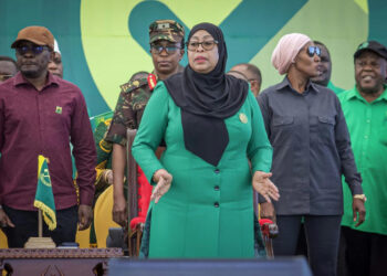 President Samia Suluhu Hassan stands at a political rally wearing a green outfit and black headscarf, surrounded by officials on stage in Tanzania