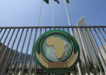 African Union headquarters gate in Addis Ababa featuring the AU emblem with a map of Africa, metal railings, and flags against a clear blue sky