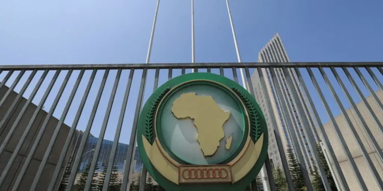 African Union headquarters gate in Addis Ababa featuring the AU emblem with a map of Africa, metal railings, and flags against a clear blue sky