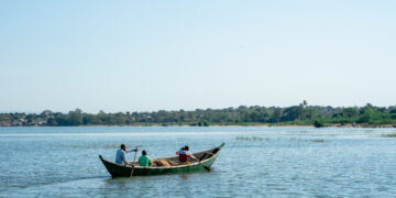Three men paddle a wooden fishing boat on a calm lake in Africa, symbolising small-scale aquaculture and the continent’s growing blue economy.