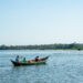 Three men paddle a wooden fishing boat on a calm lake in Africa, symbolising small-scale aquaculture and the continent’s growing blue economy.
