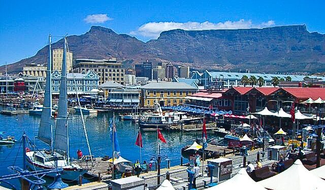 Cape Town’s V&A Waterfront with Table Mountain in the background on a clear summer day, showing boats, shops and visitors