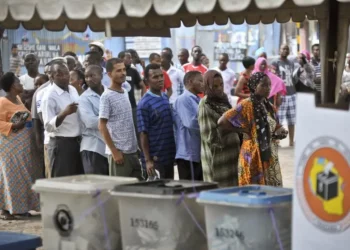 Voters queue at a polling station in Tanzania during a general election, with ballot boxes in the foreground