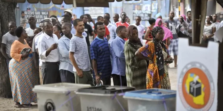 Voters queue at a polling station in Tanzania during a general election, with ballot boxes in the foreground