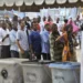 Voters queue at a polling station in Tanzania during a general election, with ballot boxes in the foreground