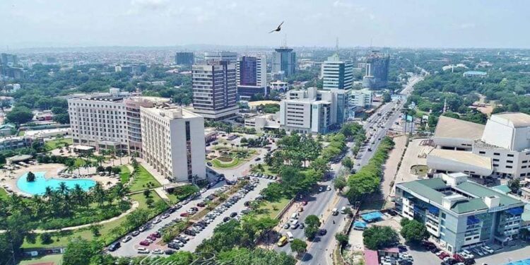 Aerial view of a modern district in Accra, Ghana, showing high-rise office buildings, busy roads, green spaces and a large hotel complex with a swimming pool.