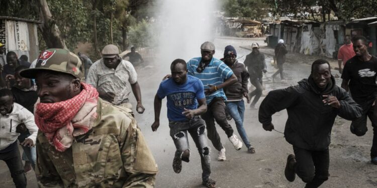 A group of Kenyan protesters run from tear gas during a confrontation with security forces on a street lined with makeshift structures