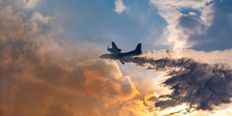 A twin-engine aircraft flying through dramatic clouds with dark smoke trailing from one side during an in-air emergency.