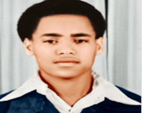 A young man with short, neat hair, wearing a collared shirt and jacket, posing for a formal portrait against a curtain backdrop.