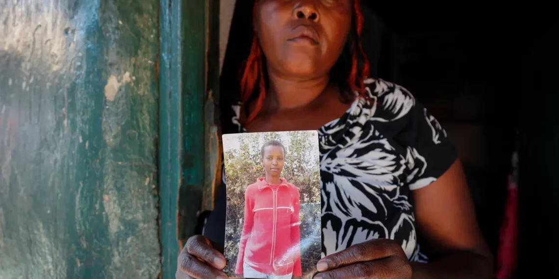 A woman stands in a doorway holding a photograph of her younger sister, Agnes Wanjiru, who was allegedly murdered in Nanyuki, Kenya, in 2012.