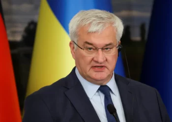 A Ukrainian government official speaks at a press conference with national flags in the background.
