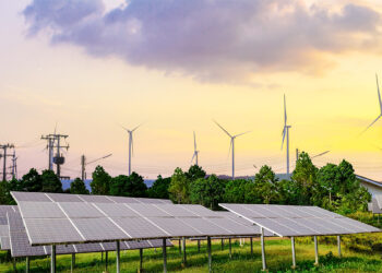 Solar panels and wind turbines generating renewable energy at sunset in a semi-rural landscape.