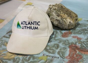 Atlantic Lithium-branded cap placed on a geological map showing the Ewoyaa lithium project area, with a lithium-bearing rock sample beside it