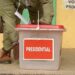 An election officer handling a sealed ballot box labelled ‘Presidential’ during voting at a polling station in Tanzania