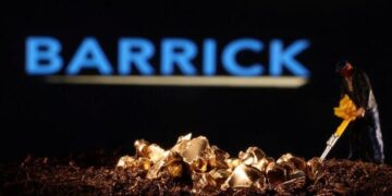 A miniature figure works beside a small pile of gold nuggets with the Barrick company logo blurred in the background.