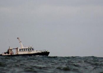 A small passenger boat tilts on choppy water under a grey sky.