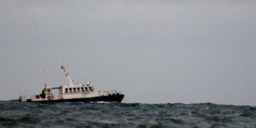 A small passenger boat tilts on choppy water under a grey sky.