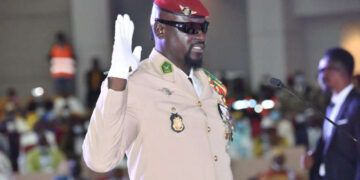 General Mamady Doumbouya raises his right hand during a swearing-in ceremony in Conakry, wearing a military uniform and red beret.