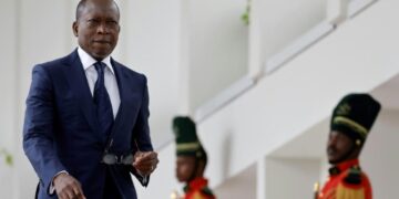 Benin’s President Patrice Talon walks past ceremonial guards in uniform at a government building.