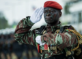 A Beninese soldier in camouflage uniform and red beret salutes during a military parade, wearing medals and tactical gear