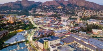 Aerial view of Mbabane’s central business district at dusk, showing office buildings, busy roads and surrounding mountains in Eswatini.