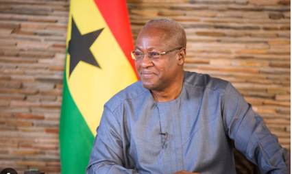 Ghana’s President seated during an official interview, with the national flag visible in the background