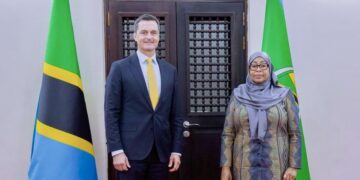 A senior Tanzanian official stands beside a visiting US diplomat, with Tanzania flags behind them during a formal meeting.
