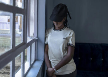 Young Maasai woman stands by a window in Narok county, reflecting on surviving female genital mutilation carried out during her childhood in rural Kenya