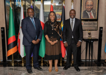 Three executives stand side by side in a formal setting with African national flags behind them at an aviation meeting.