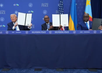 Three leaders hold signed documents at a Washington ceremony marking a peace agreement between the United States, Rwanda and the Democratic Republic of Congo, with national flags displayed behind them.