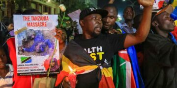 Protesters holding candles and placards during a nighttime demonstration condemning violence in Tanzania, with one sign reading ‘The Tanzania Massacre’