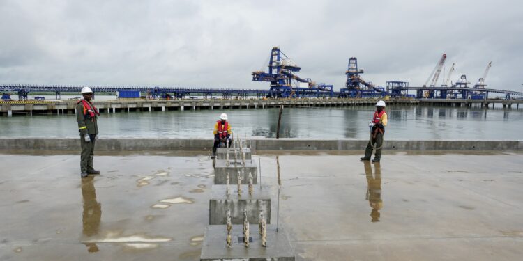 Workers stand on the quay at Guinea’s Morebaya port as bulk handling infrastructure and ship loaders line the waterfront, highlighting the country’s expanding iron ore export capacity