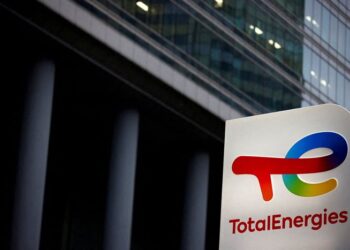 A TotalEnergies logo sign outside a modern glass corporate building.