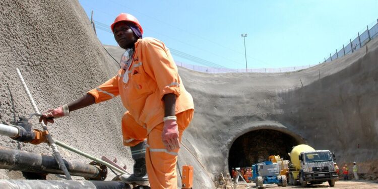 Construction worker in protective gear stands beside pipes at the entrance of the Gautrain underground tunnel in Gauteng, South Africa