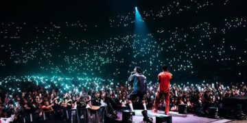Afrobeats artists perform on stage before a packed crowd holding up phone lights at a live concert, highlighting the global rise of Nigeria’s music industry