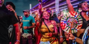 A crowd of young festivalgoers dance and celebrate at a vibrant outdoor Detty December event at night in West Africa