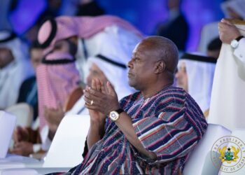 President Mahama applauds during an international conference, wearing traditional Ghanaian attire, with global delegates seated around him