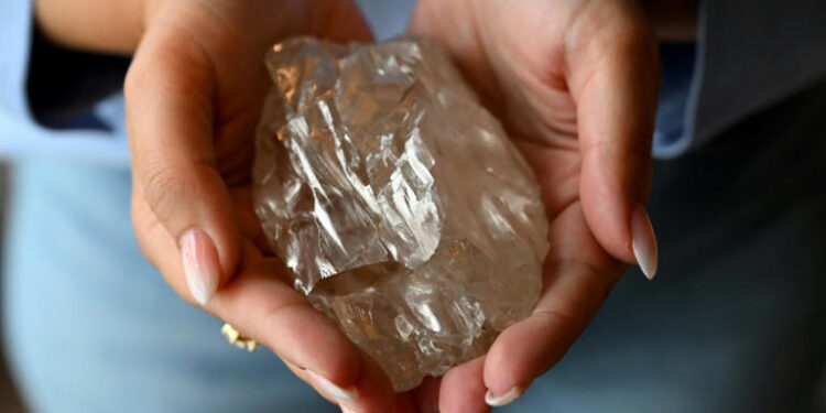 Hand holding a large rough diamond discovered in Botswana amid global market slowdown.