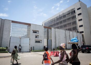 People walk past the Bank of Ghana headquarters in Accra following the central bank’s decision to cut its benchmark interest rate to 15.5 percent.