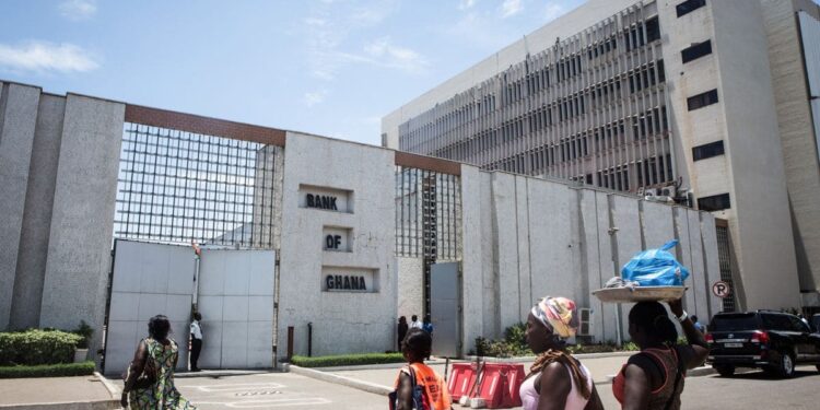 People walk past the Bank of Ghana headquarters in Accra following the central bank’s decision to cut its benchmark interest rate to 15.5 percent.