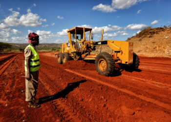 Road construction underway in Kenya as a grader works on a red earth highway project, highlighting government-funded infrastructure development