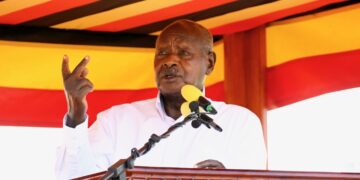 African head of state addresses a public rally from a podium, gesturing while speaking against a backdrop of national colours