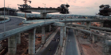 Construction underway at the Pokuase Interchange in Accra, Ghana, showing elevated road ramps and traffic passing beneath unfinished flyovers