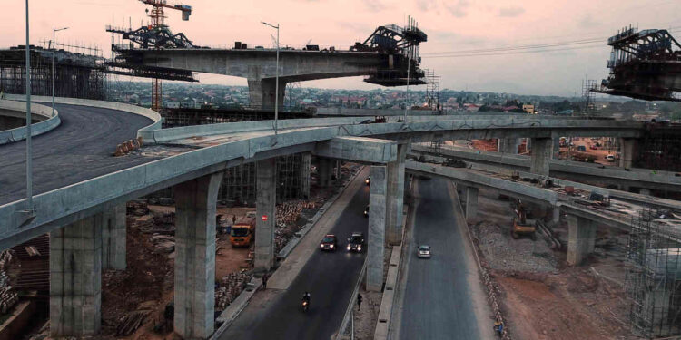 Construction underway at the Pokuase Interchange in Accra, Ghana, showing elevated road ramps and traffic passing beneath unfinished flyovers