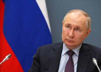 Senior Russian official seated at a formal meeting with national flags displayed behind him