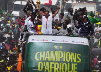 Senegal players celebrate Africa Cup of Nations victory atop open-top bus in Dakar holding trophy as crowds line the streets