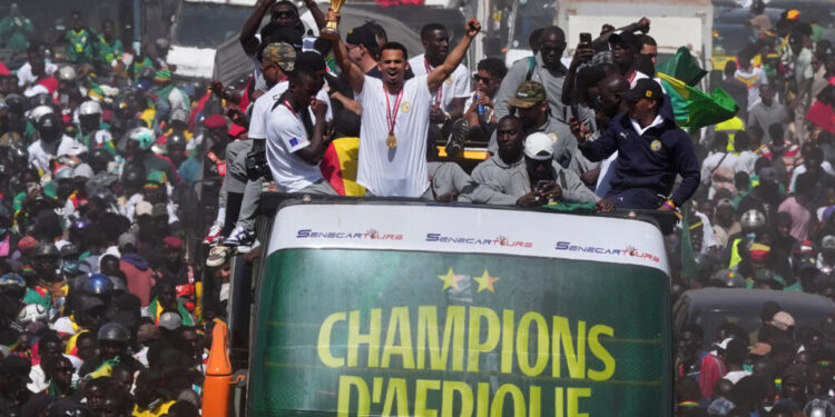 Senegal players celebrate Africa Cup of Nations victory atop open-top bus in Dakar holding trophy as crowds line the streets