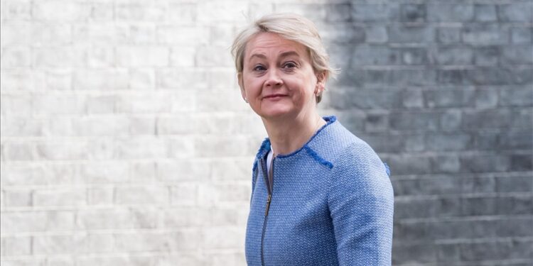 British foreign secretary Yvette Cooper standing in front of a grey brick wall in formal attire