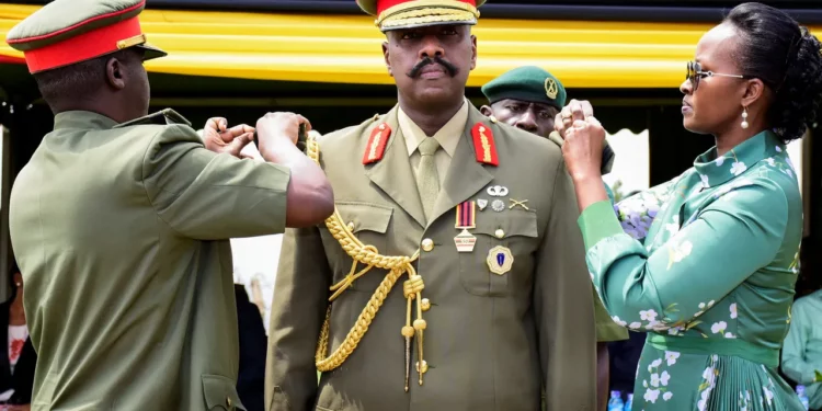 A senior Ugandan army officer in formal dress uniform being adorned with a ceremonial gold aiguillette by two officials during a military event