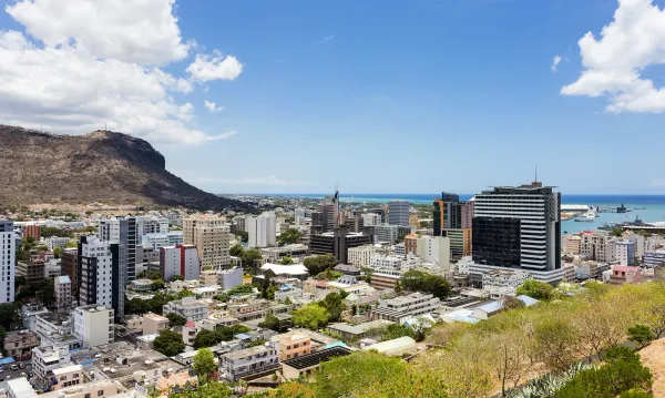 Aerial view of Port Louis, Mauritius, showing modern high-rise buildings, the harbour, and Le Pouce mountain under a clear blue sky